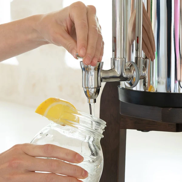 Person filling glass jar with lemon slice from Woder Clearbrook large countertop gravity water filter stainless steel spigot